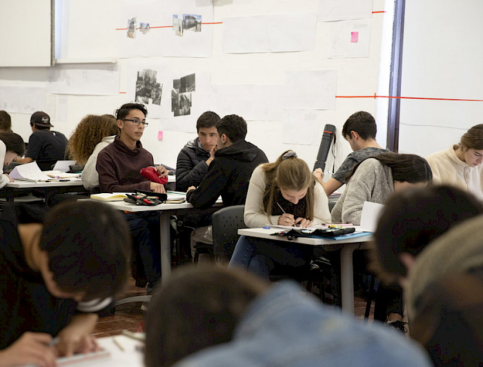 Grupo de estudiantes sentados en escritorios en una sala de clases.